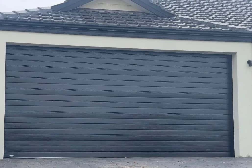 A closed charcoal woodgrain double sectional garage door in a cream rendered wall