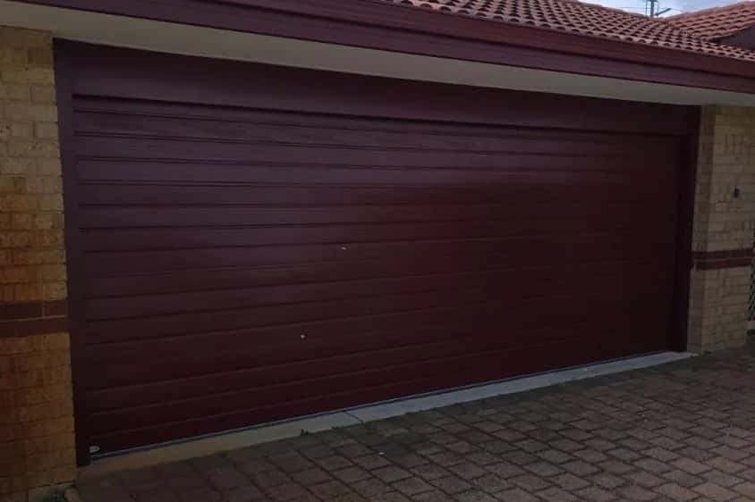 A dark maroon ribbed sectional garage door, closed, on a brick house with a tiled roof