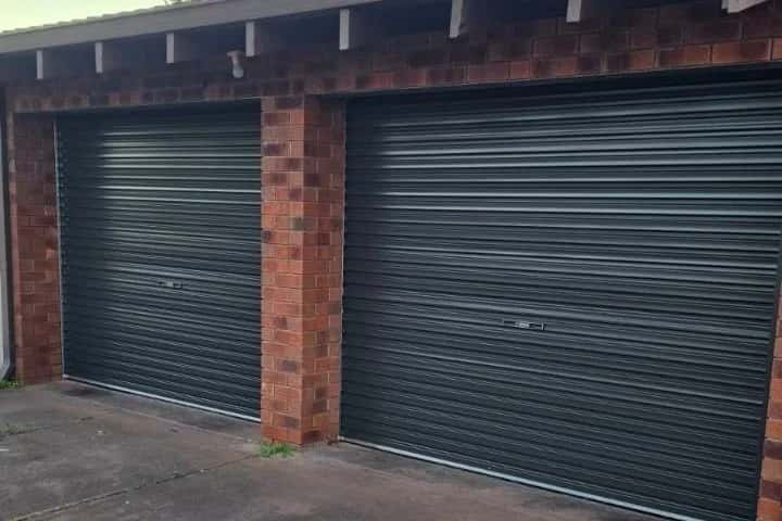 Two dark charcoal roller doors closed on a red brick double garage under a timber eave