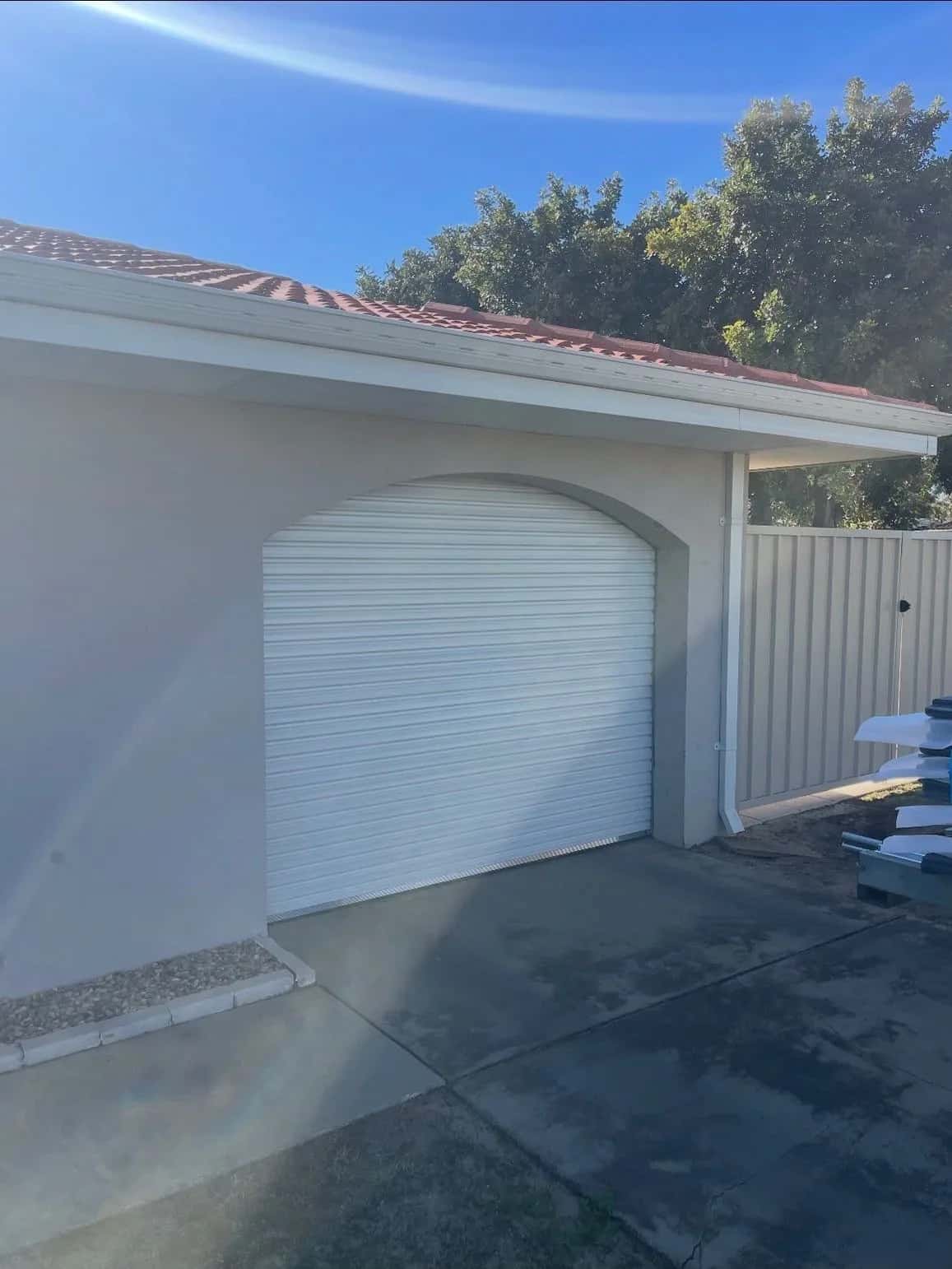 A white roller door inside an arched rendered carport opening