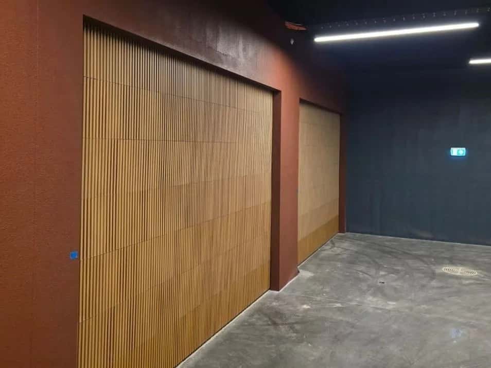 Two closed garage doors faced in vertical timber-look slats, set into a dark red wall in an underground carpark