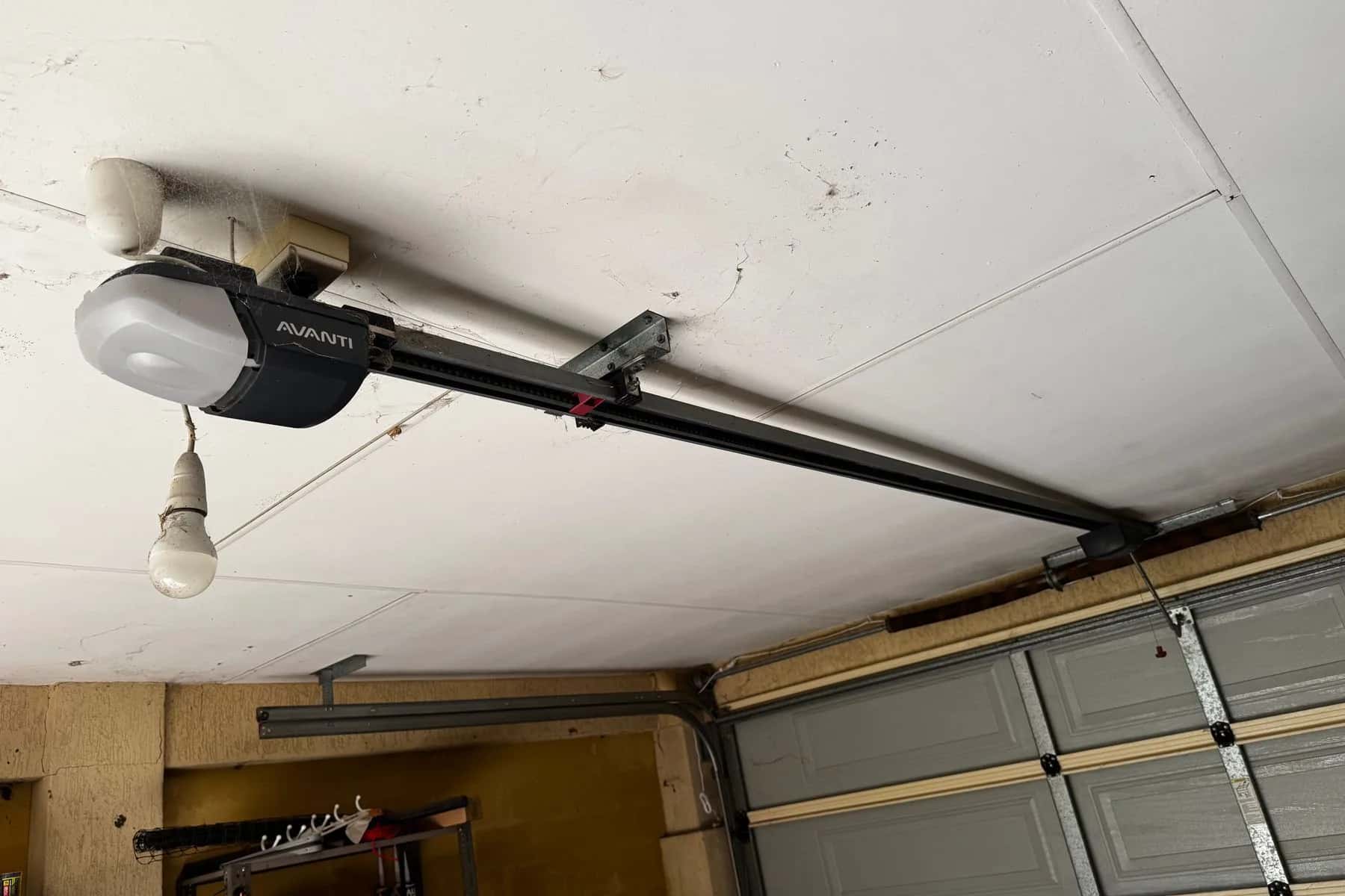 An old ceiling-mounted garage door opener with a bare bulb hanging beside it