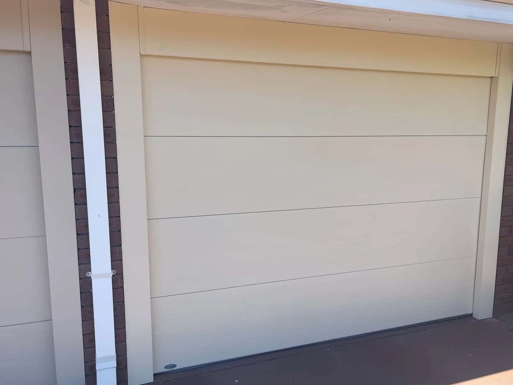 A new cream flat-panel single sectional garage door with matching jamb covers beside a brick pier