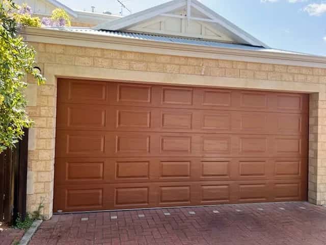 A terracotta raised-panel double sectional garage door on a limestone house with a flowering vine
