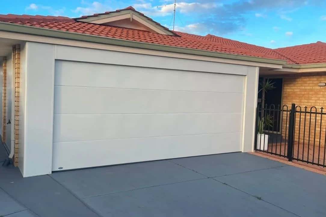A new white flat-panel double sectional garage door under a terracotta tile roof at sunset