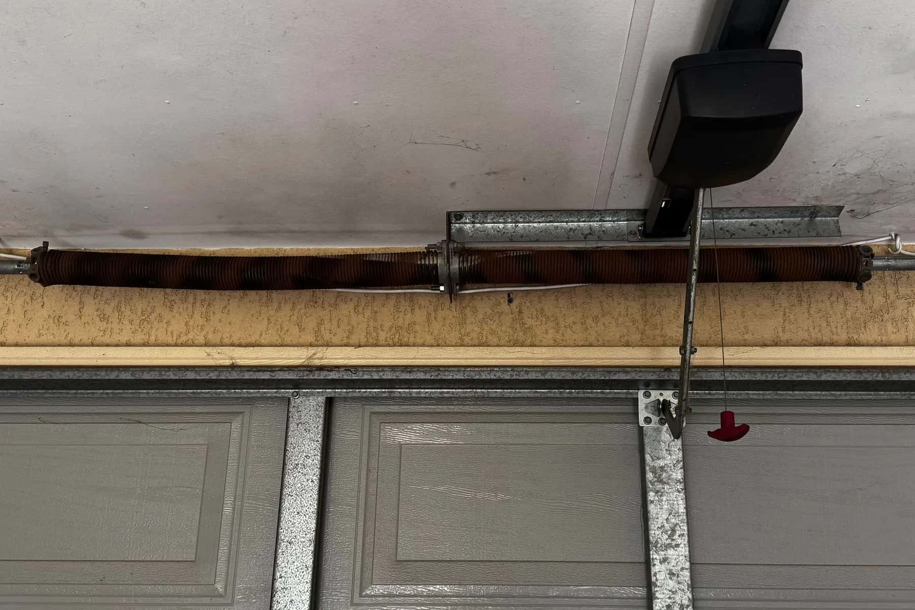 A rusted torsion spring on the shaft above a grey sectional door