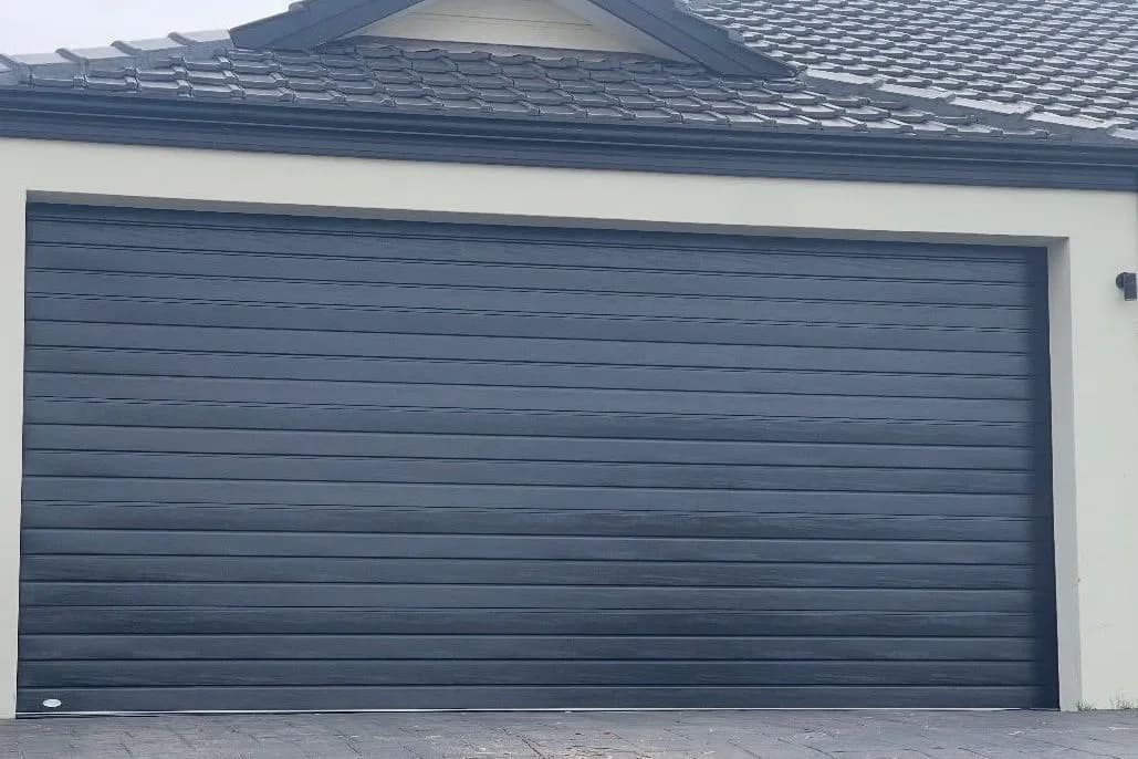 A closed charcoal woodgrain double sectional garage door in a cream rendered wall