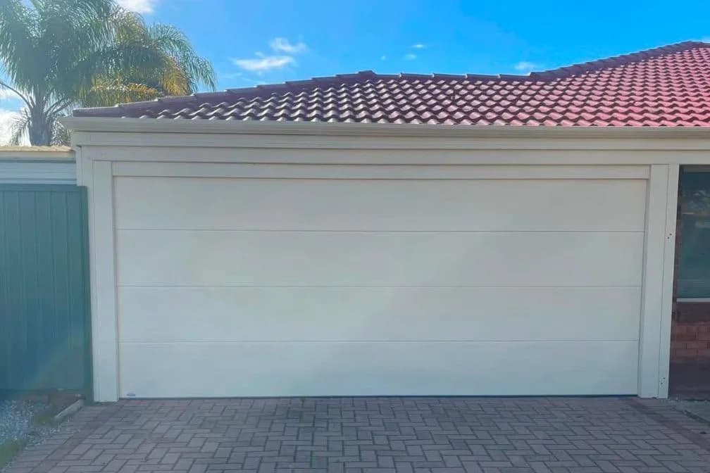 A cream sectional garage door on a rendered house with a terracotta tile roof and a brick paved driveway