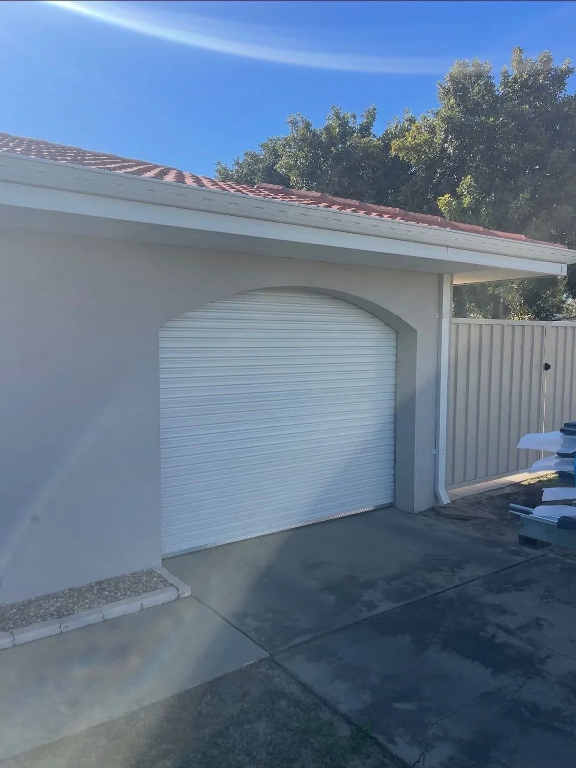 A white roller door inside an arched rendered carport opening