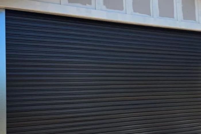 A black corrugated roller door, closed, beneath a cream fascia