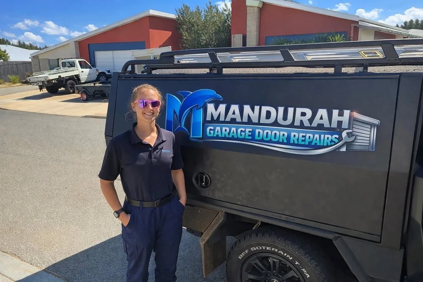 A technician in a navy polo standing beside the sign-written ute on a sunny suburban street