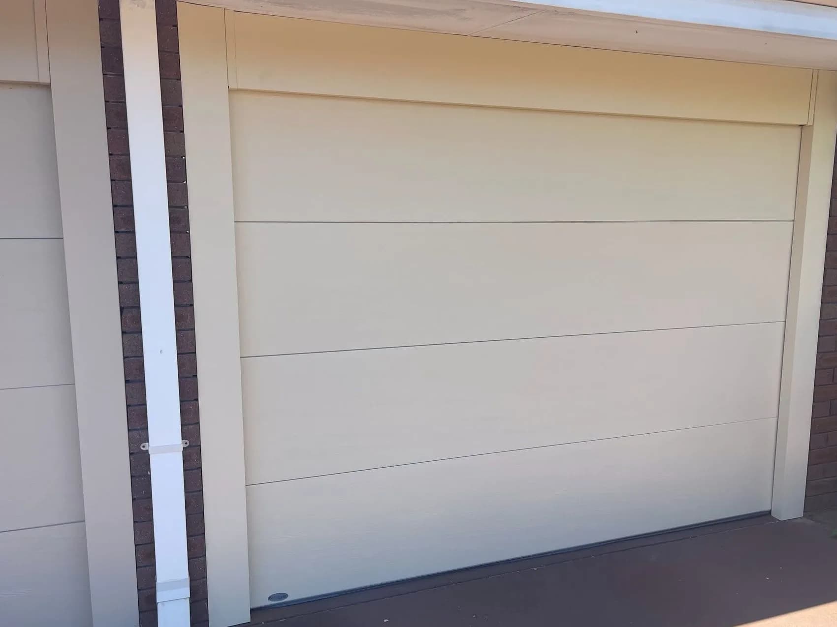 A new cream flat-panel single sectional garage door with matching jamb covers beside a brick pier