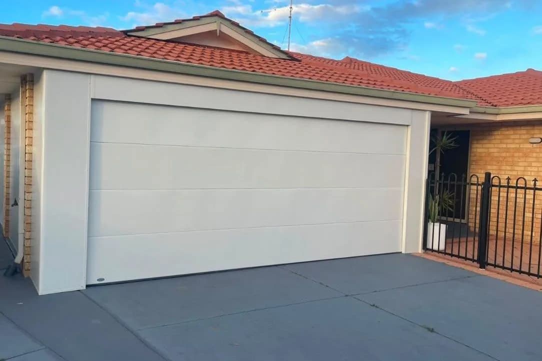 A new white flat-panel double sectional garage door under a terracotta tile roof at sunset