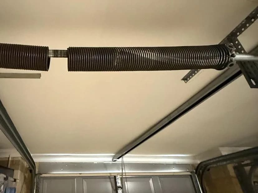 A torsion spring snapped in two on the shaft above a sectional garage door, a clear gap between the broken halves