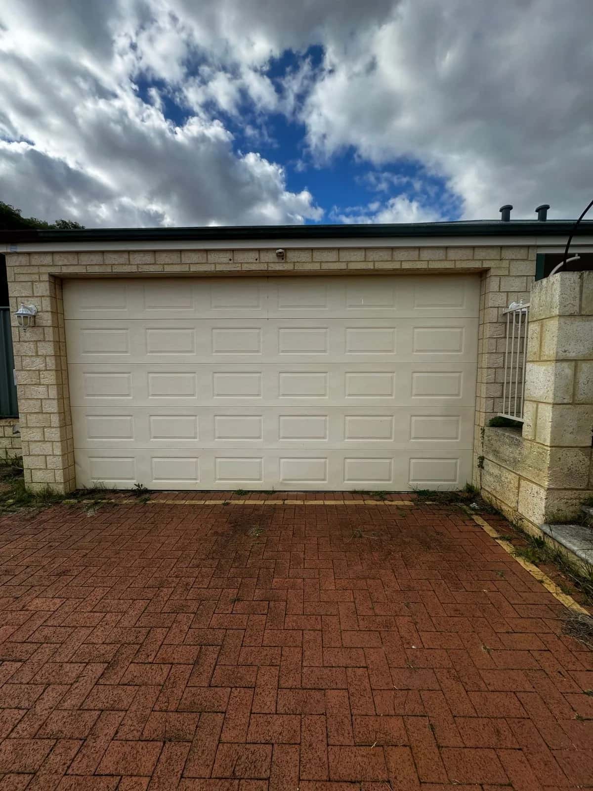 A cream sectional door on a limestone-block house with a red brick driveway