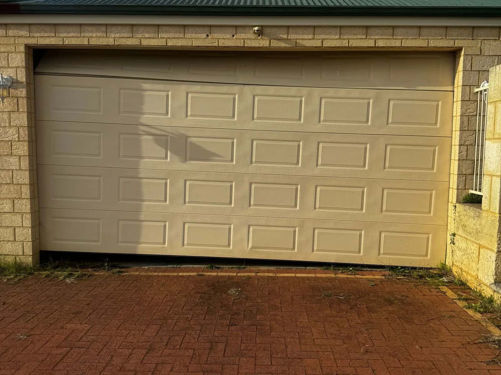 A cream sectional door sitting crooked in its opening after a lift cable snapped