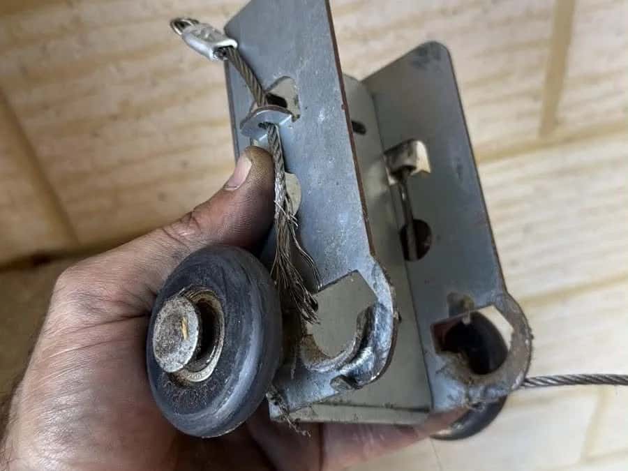 A worn bottom bracket and roller held in a hand, its lift cable frayed through