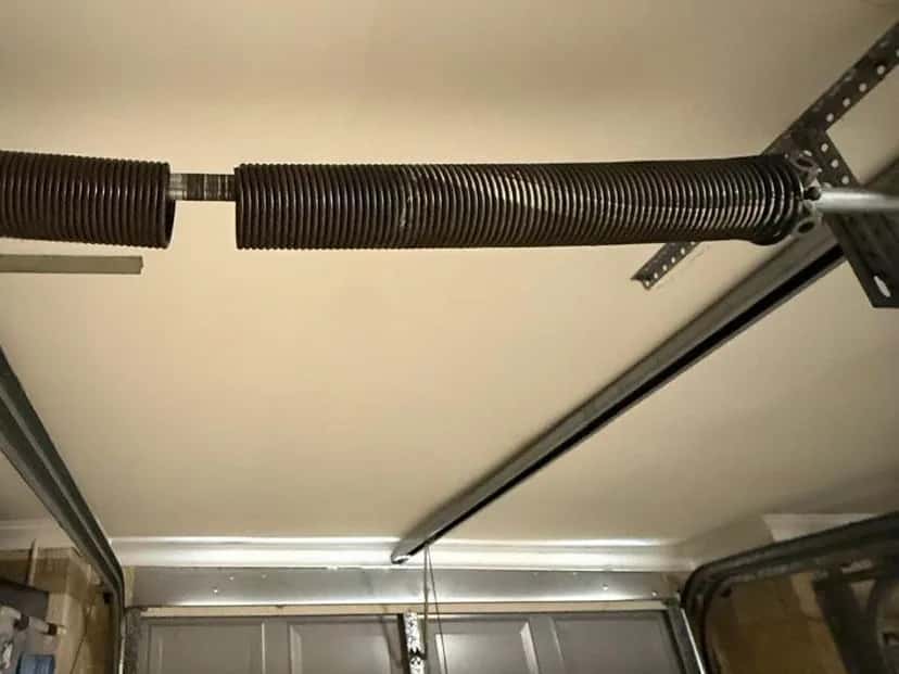 A torsion spring snapped in two on the shaft above a garage door, a gap open between the halves